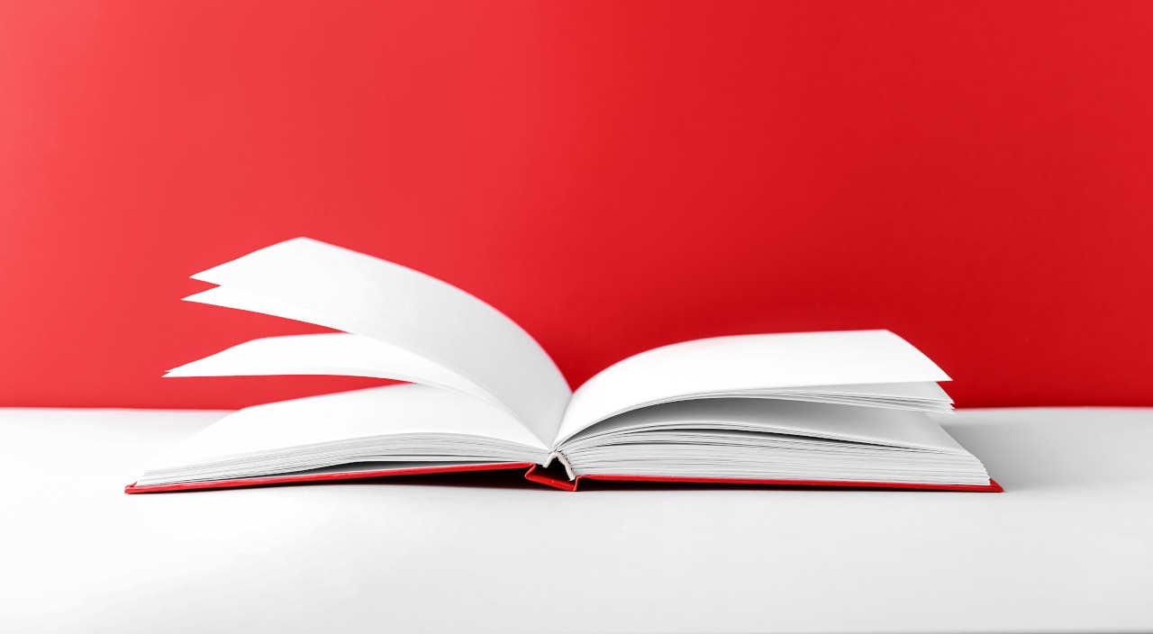 Ein auf einem weißem Tisch liegendes, aufgeschlagenes Buch vor einem roten Hintergrund
